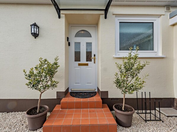 A house with a white door, two potted trees, and a window. - 2 Bed in Saundersfoot (oc-94207) (Saundersfoot)