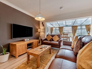 A modern living room with a flat-screen TV, wooden furniture, a leather sofa, and a large window with curtains. - 2 Bed in Saundersfoot (oc-94207) (Saundersfoot)
