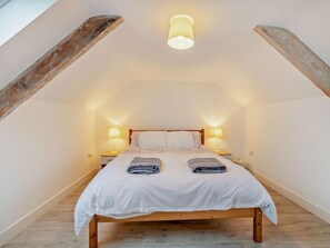 Un dormitorio con techo inclinado, una cama con sábanas blancas, dos lámparas de noche y un cabecero de madera.