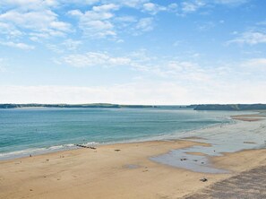 Een uitgestrekt zandstrand met rustig water, heuvels in de verte en een heldere lucht.