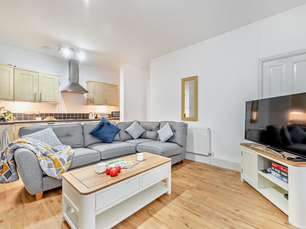 Een moderne woonkamer met een grijze bank, een houten salontafel en een flatscreen televisie.
