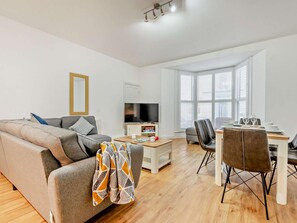 Ein modernes Wohnzimmer mit Sofa, Couchtisch, Fernseher und Essbereich mit Stühlen und Tisch.
