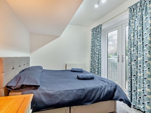 Ein Schlafzimmer mit einem Bett, einer Heizung und Blick durch ein Fenster mit Vorhängen.