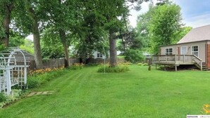 A residential backyard with a lawn, a wooden deck, and a house with a porch.