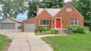 A two-story brick house with a red front door, a garage, and a well-maintained lawn.