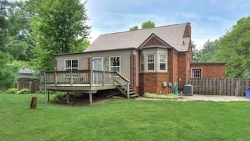 Une maison à deux étages avec une terrasse, une cour arrière clôturée et une cheminée en briques.