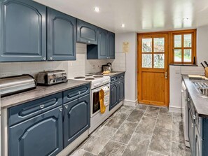 A kitchen with blue cabinets, a stove, a toaster, and a wooden door. - 3 Bed in Llandysul (oc-94117) (Rhydlewis)