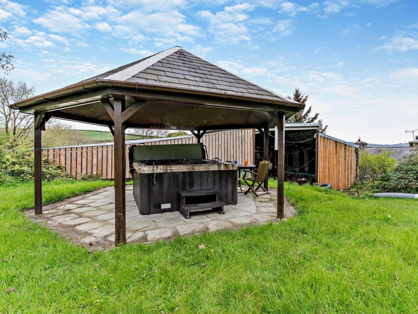 Un espace barbecue extérieur abrité, équipé d’un gril, de sièges et d’une clôture en bois en arrière-plan.