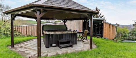 A covered outdoor barbecue area with a grill, seating, and a wooden fence in the background.