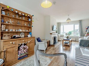 A cozy living room with a fireplace, wooden shelves with decorative items, a comfortable sofa, and a large window with a view. - 3 Bed in Seaview (oc-94257) (Saint Helens)