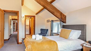 Ein Schlafzimmer mit einem Bett, einem Sessel, einem Nachttisch, einem Spiegel und einem Holzbalken an der Decke.