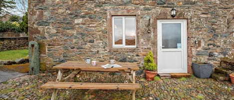 Un bâtiment en pierre avec un banc en bois et une table, une porte et une fenêtre.