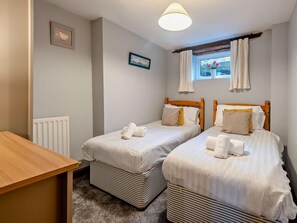 Ein Zimmer mit zwei Betten, einem Holztisch, einem Heizkörper und einem Fenster mit Vorhängen.