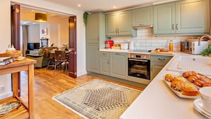 A modern kitchen with light green cabinets, a central island, and a dining area with a wooden table and chairs. - 2 Bed in Middlesbrough (oc-94220) (Great Broughton)