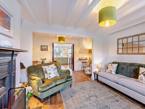 Ein Wohnzimmer mit Kamin, zwei Sofas, einem Teppich und einer durchgehenden Tür erkennbaren Küche.