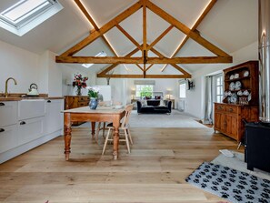 Een ruime keuken met houten balken, een eethoek en een woonkamer met een bank.
