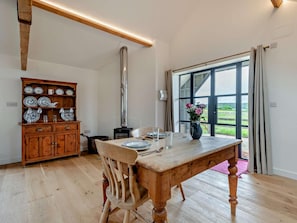 A dining area with a wooden table, chairs, a cabinet with dishes, and a view through a large window. - 1 Bed in Blandford Forum (oc-94279) (Okeford Fitzpaine)
