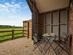 A patio with a table and chairs, a wooden fence, and a view of a green field. - 1 Bed in Blandford Forum (oc-94279) (Okeford Fitzpaine)