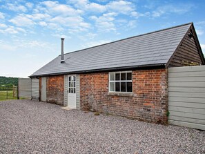 A small brick building with a sloped roof, a chimney, and a gravel driveway. - 1 Bed in Blandford Forum (oc-94279) (Okeford Fitzpaine)