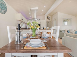 A dining area with a wooden table set for four, a vase of flowers, and a clock on the wall.