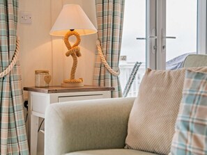A room with a sofa, a lamp with a rope base, a window with curtains, and a view of a building outside.