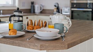 Eine Küchenarbeitsplatte mit Frühstücksartikeln, darunter Croissants, eine Schüssel mit Müsli und ein Orangensaftkrug.
