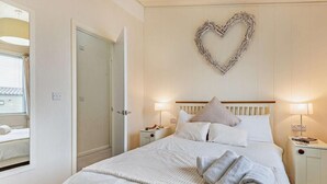 Ein Schlafzimmer mit einem Bett, zwei Nachttischen, einer herzförmigen Dekoration an der Wand und einem Spiegel.