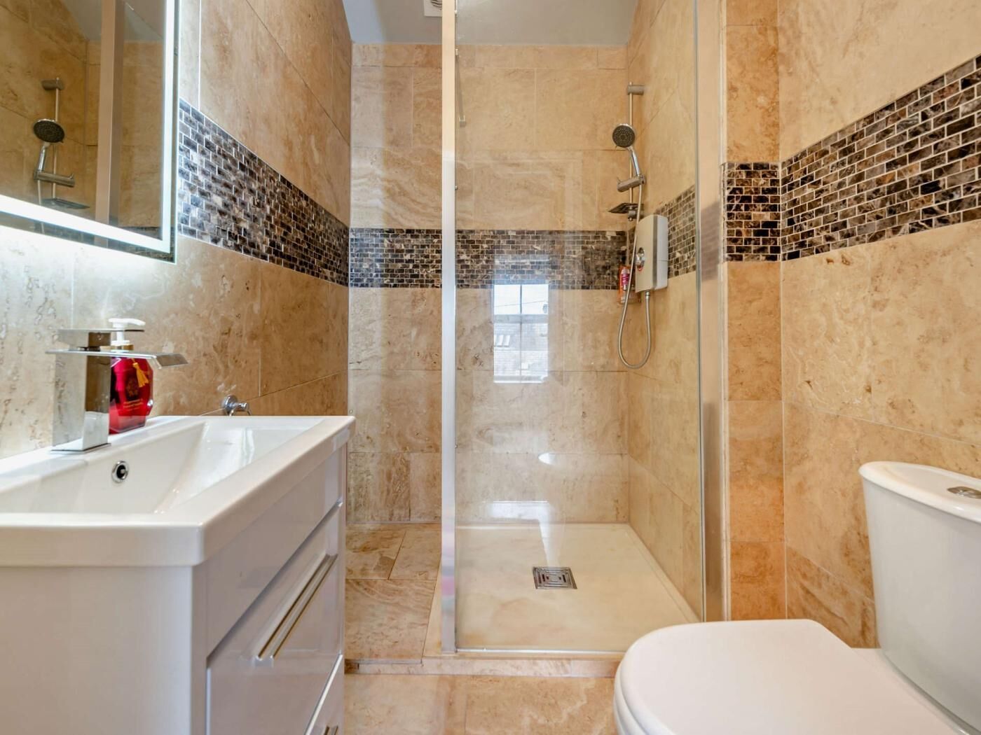 Un baño con ducha de vidrio, lavamanos blanco y un inodoro.