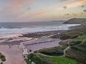 A coastal landscape with a beach, rocky shoreline, and a path leading to a grassy area. - 3 Bed in Tenby (oc-94186) (Saint Florence)