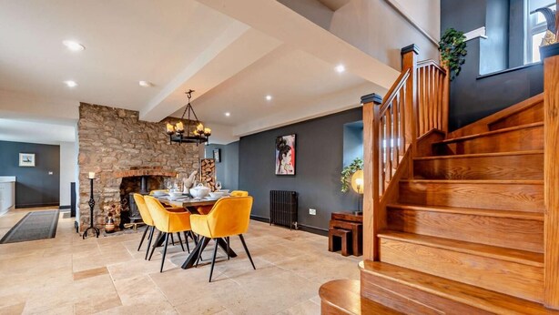 Amplia sala de estar con chimenea de piedra, una mesa de comedor con sillas y una escalera de madera.