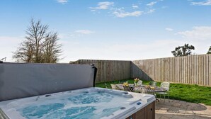 Un jacuzzi con terraza de madera, una mesa con sillas y una valla de madera al fondo.