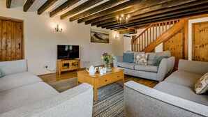 Una sala de estar con televisor, sofá, mesa de centro y una escalera.