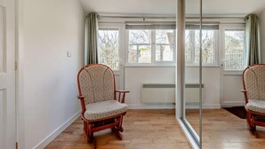 Ein Zimmer mit Holzboden, einem großen Spiegel, zwei Holzstühlen und einem Fenster mit Blick auf Bäume.