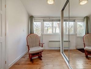 A room with wooden flooring, a large mirror, two wooden chairs, and a window with a view of trees.