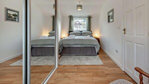 Ein Schlafzimmer mit einem Bett, Nachttischlampen, einem Spiegel, einem Fenster und einer Tür.
