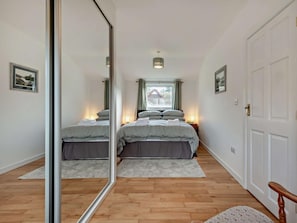 A bedroom with a bed, bedside lamps, a mirror, a window, and a door.