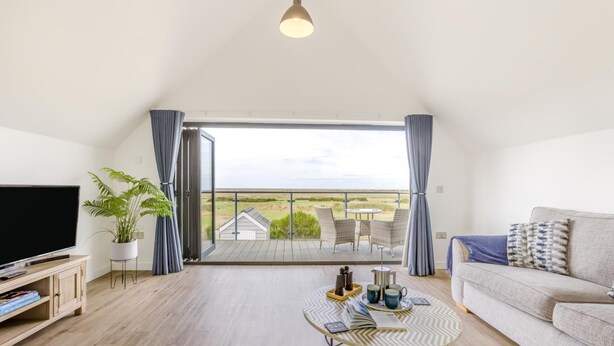 Ein geräumiges Wohnzimmer mit Flachbildfernseher, Couch, Couchtisch und einem Balkon mit Blick auf die Landschaft.