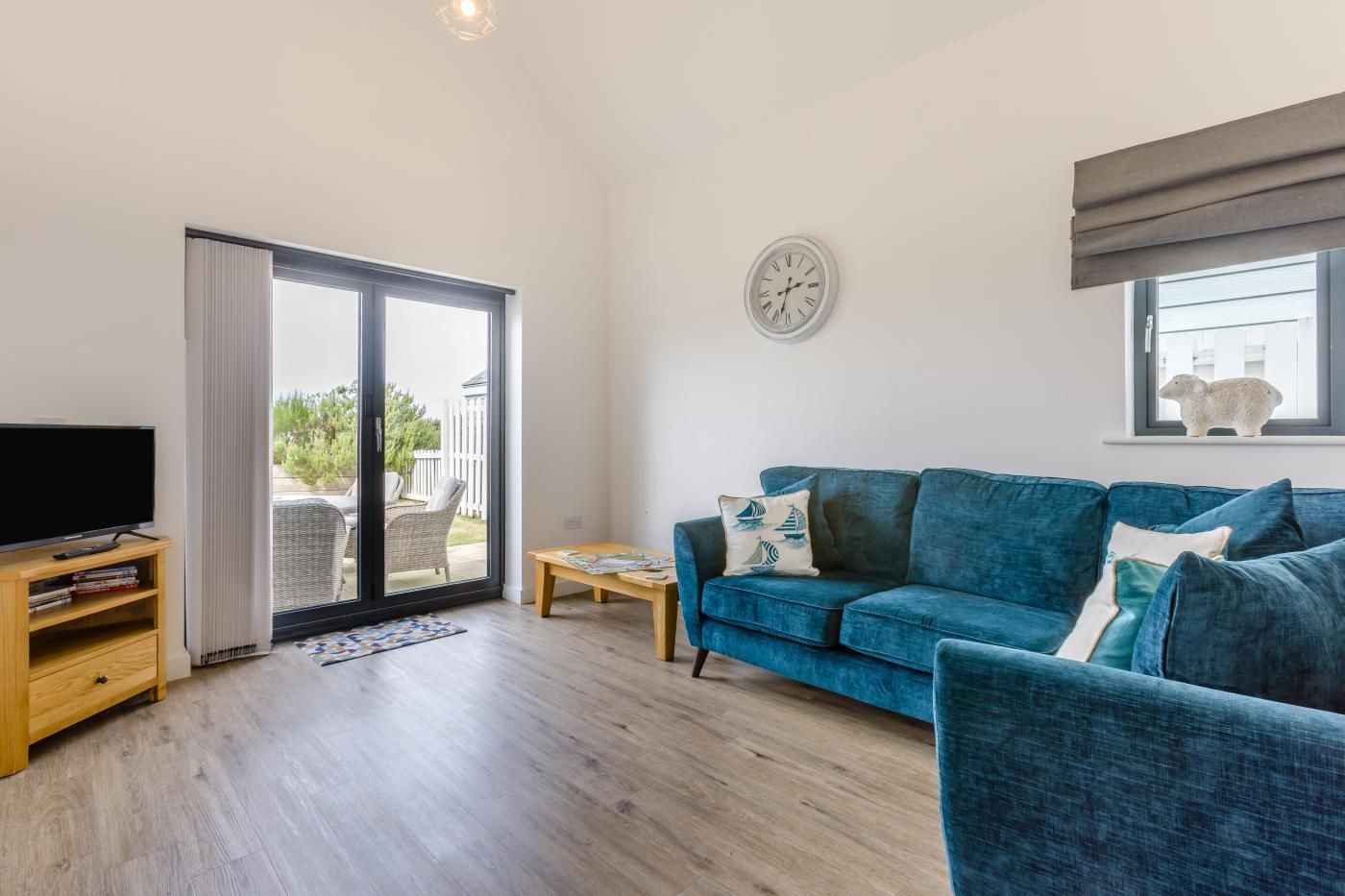 A living room with a blue sofa, a television, and a sliding glass door leading to an outdoor area.