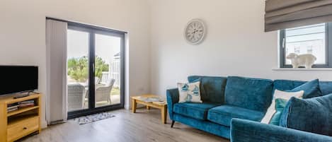 Ein Wohnzimmer mit einem blauen Sofa, einem Fernseher und einer Glastür, die zu einem Außenbereich führt.