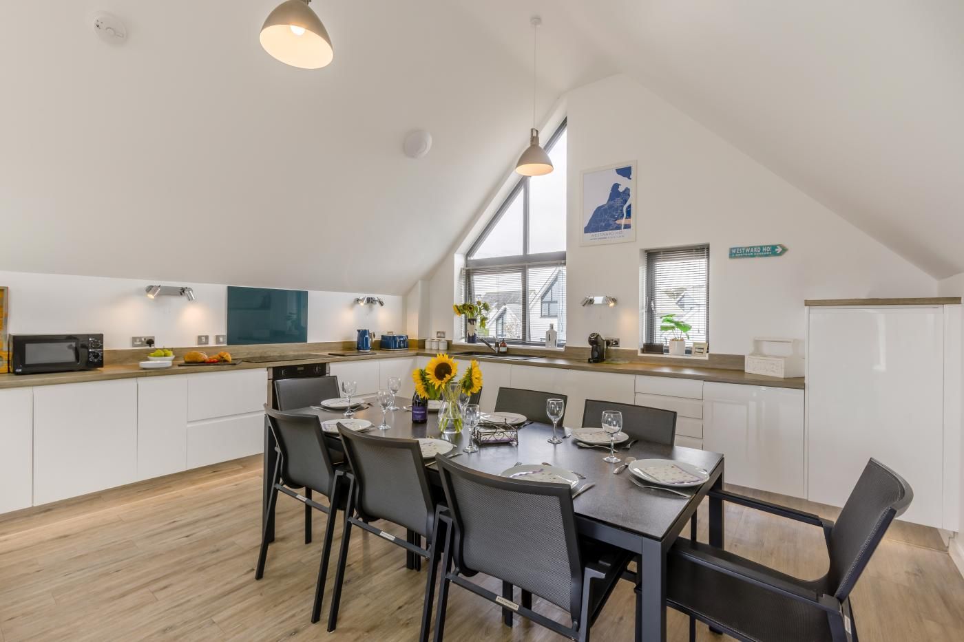 Een moderne keuken met een eethoek, voorzien van een magnetron, spoelbak en een tafel gedekt voor vier personen.