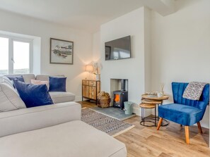 A modern living room with a sofa, a blue armchair, a fireplace, a TV, and a painting on the wall. - 4 Bed in Fowey (oc-77595) (Fowey)