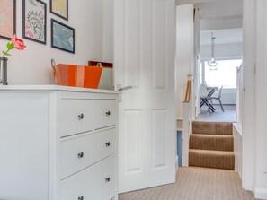 A hallway with a white door, a staircase with patterned carpet, and a dining area with a table and chairs. - 4 Bed in Fowey (oc-77595) (Fowey)