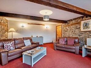 Ein gemütliches Wohnzimmer mit zwei Ledersofas, einem Couchtisch, einer Steinwand und einem Holzbalken an der Decke.