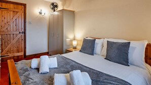 Et soveværelse med seng, puder, et natbord, en lampe, en ventilator og et klædeskab.