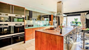 A modern kitchen with stainless steel appliances, a wooden island, and a bar area with stools. - 4 Bed in Bognor Regis (oc-81446) (Bognor Regis)