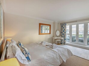 Ein Hotelzimmer mit einem großen Bett, einem Schreibtisch mit Spiegel und Meerblick durch große Fenster.