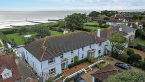 A white two-story house with a tiled roof, a driveway, and a car parked in the front. - 4 Bed in Bognor Regis (oc-81446) (Bognor Regis)