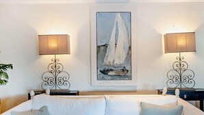 A room with a white sofa, two wall-mounted lamps, and a framed painting of a sailboat. - 4 Bed in Bognor Regis (oc-81446) (Bognor Regis)