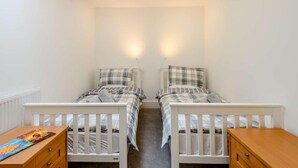 Quarto duplo com duas camas de solteiro, cômoda de madeira e radiador.