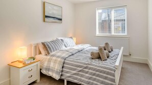 Quarto com cama, mesa de cabeceira, luminária, janela e um quadro na parede.
